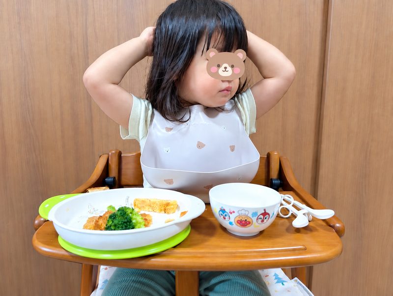 2歳の娘が食卓で手を頭に上げ、食事が進んでいない様子